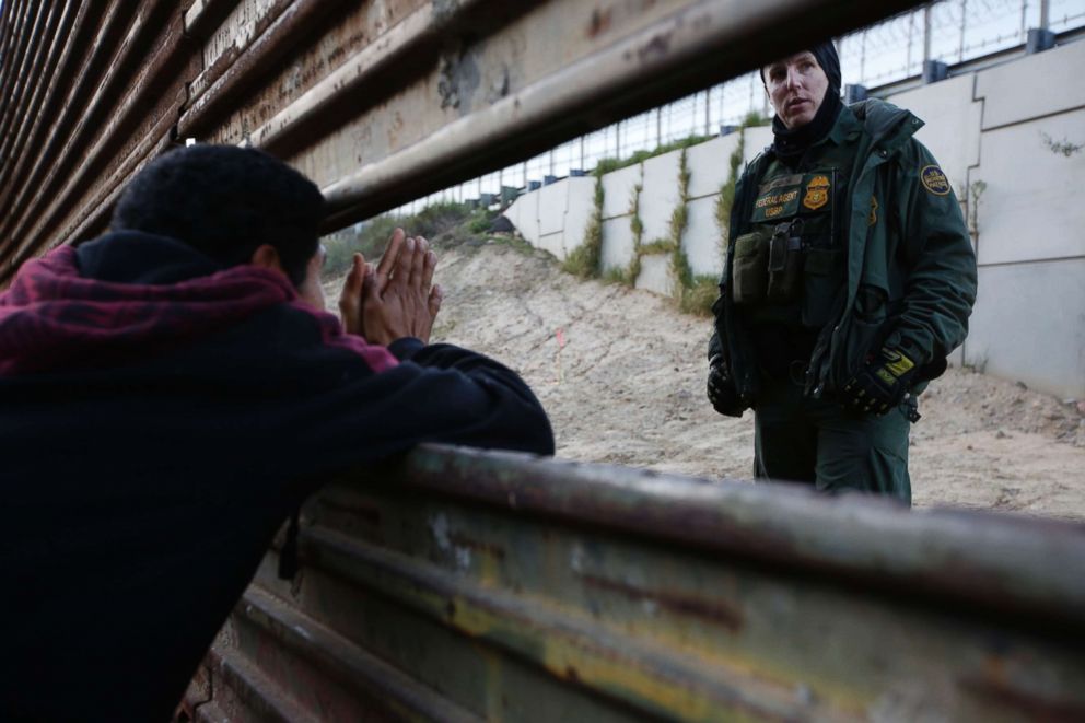 PHOTO: A Honduran migrant, left, talks with a Border Patrol agent as he tries to cross over the U.S. border wall to San Diego, California, from Playas in in Tijuana, Mexico, Dec. 15, 2018.