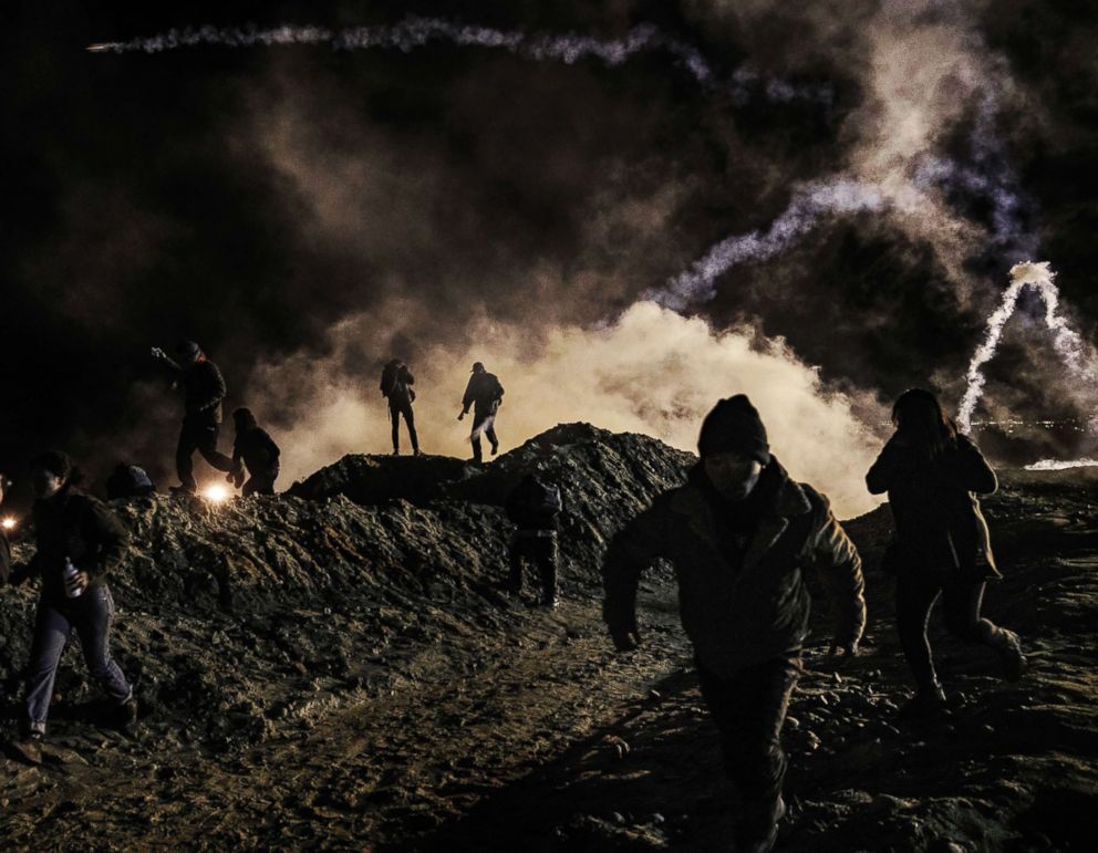 PHOTO: Migrants run as tear gas is thrown by U.S. Border Protection officers to the Mexican side of the border fence after they climbed the fence to get to San Diego, Calif., from Tijuana, Mexico, Jan. 1, 2019.