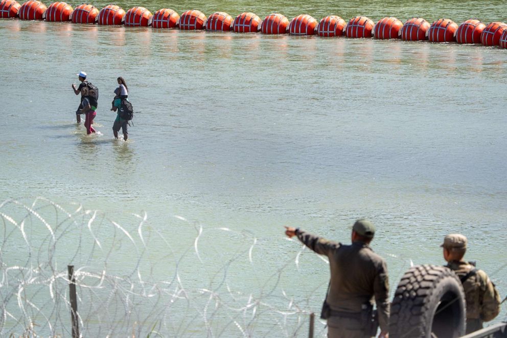 PHOTO: Texas Department of Public Safety highway patrol troopers look over the Rio Grande as migrants walk by a string of buoys placed on the water along the Rio Grande border with Mexico in Eagle Pass, Texas, on July 15, 2023.