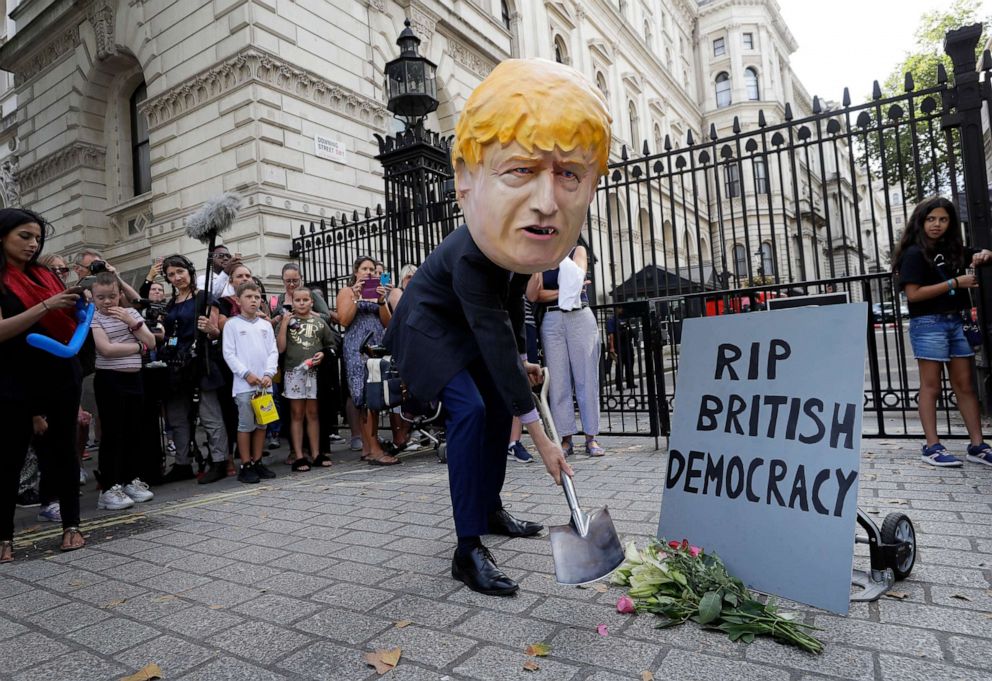 PHOTO: A man in a giant Boris Johnson head digs a grave at the foot of a pretend tombstone outside Downing Street in London, Aug. 28, 2019.
