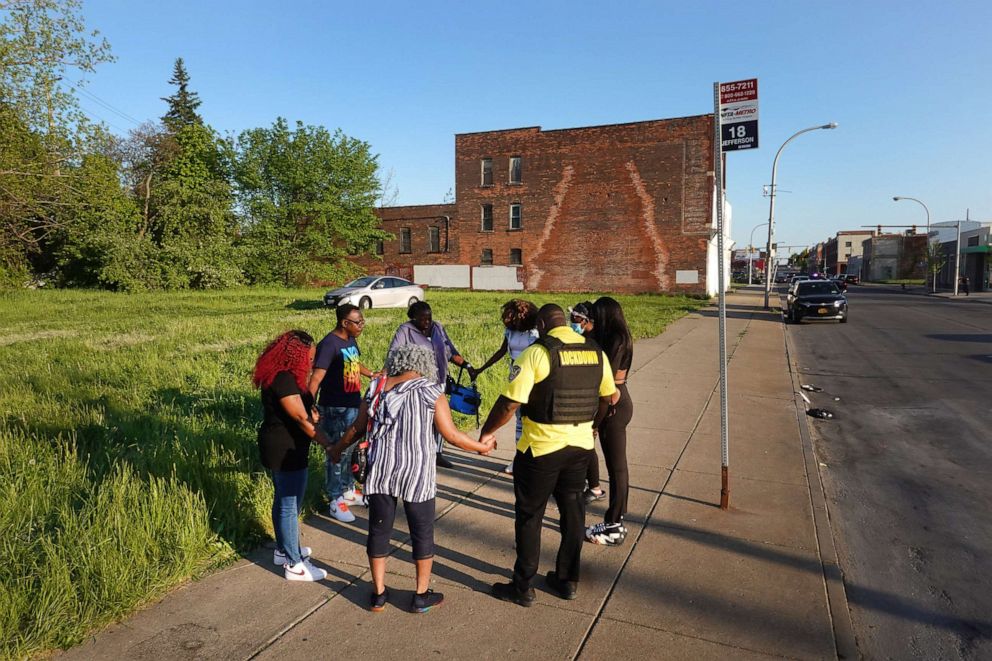 PHOTO: People pray across the street from Tops supermarket on May 15, 2022 in Buffalo, New York, the day after 10 people were killed and three wounded when a gunman opened fire.