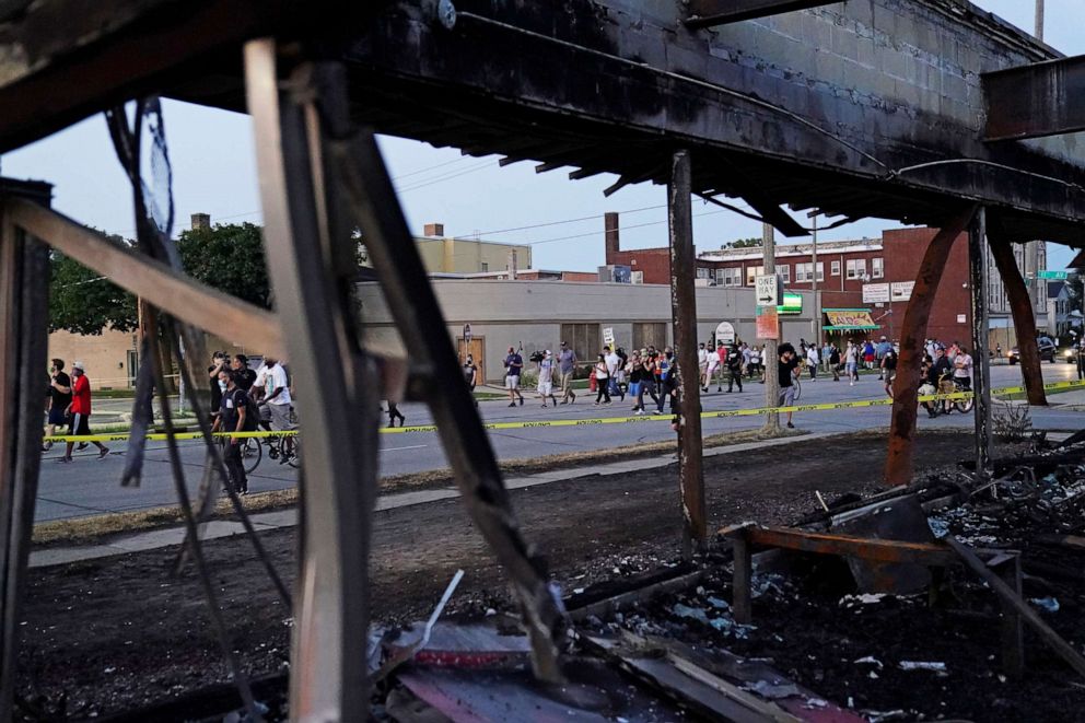 PHOTO: Demonstrators march past a burned out building damaged during protests against the police shooting of Jacob Blake in Kenosha, Wisconsin, on Aug. 26, 2020.