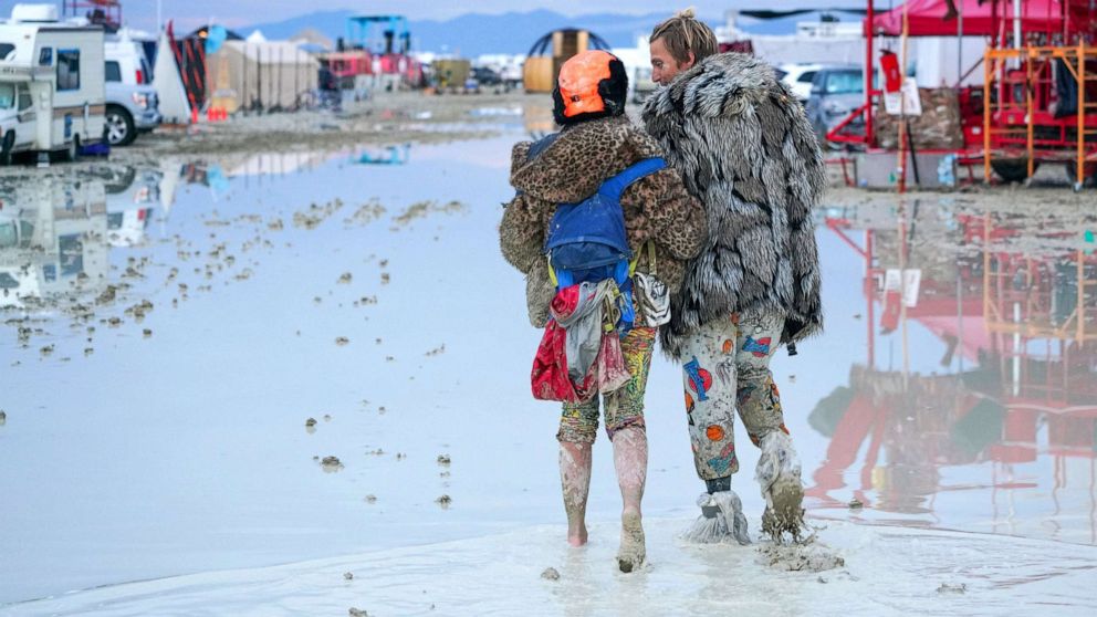 PHOTO: Dub Kitty and Ben Joos, of Idaho and Nevada, walk through the mud on Sept. 2, 2023, at Burning Man after a night of dancing with friends.