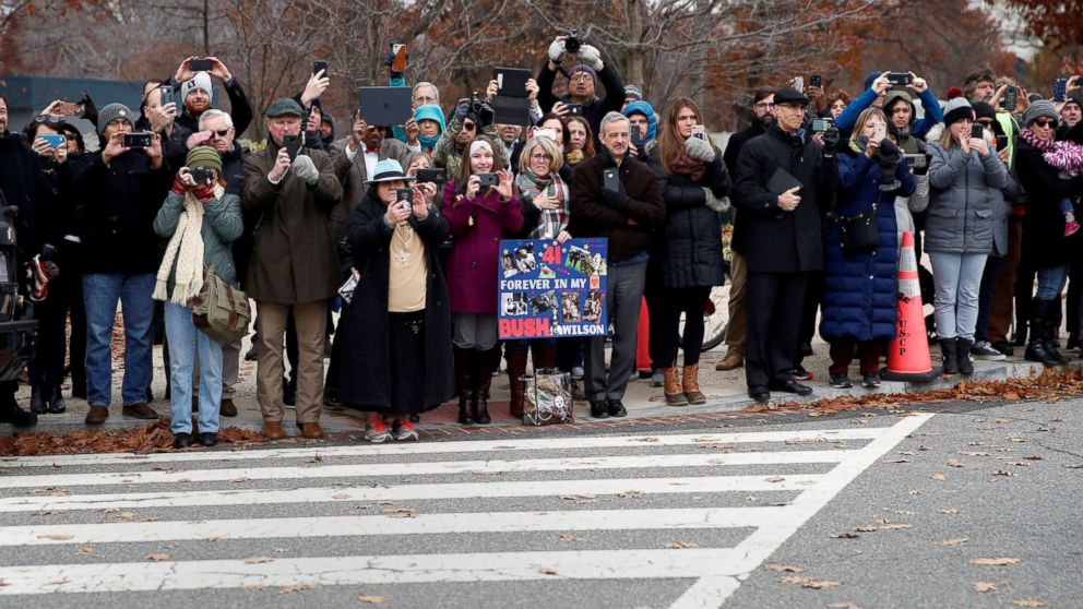 PHOTO: People line the street as the hearse carrying the flag-draped casket of former President George H.W. Bush heads to a State Funeral at the National Cathedral, Dec. 5, 2018, in Washington.