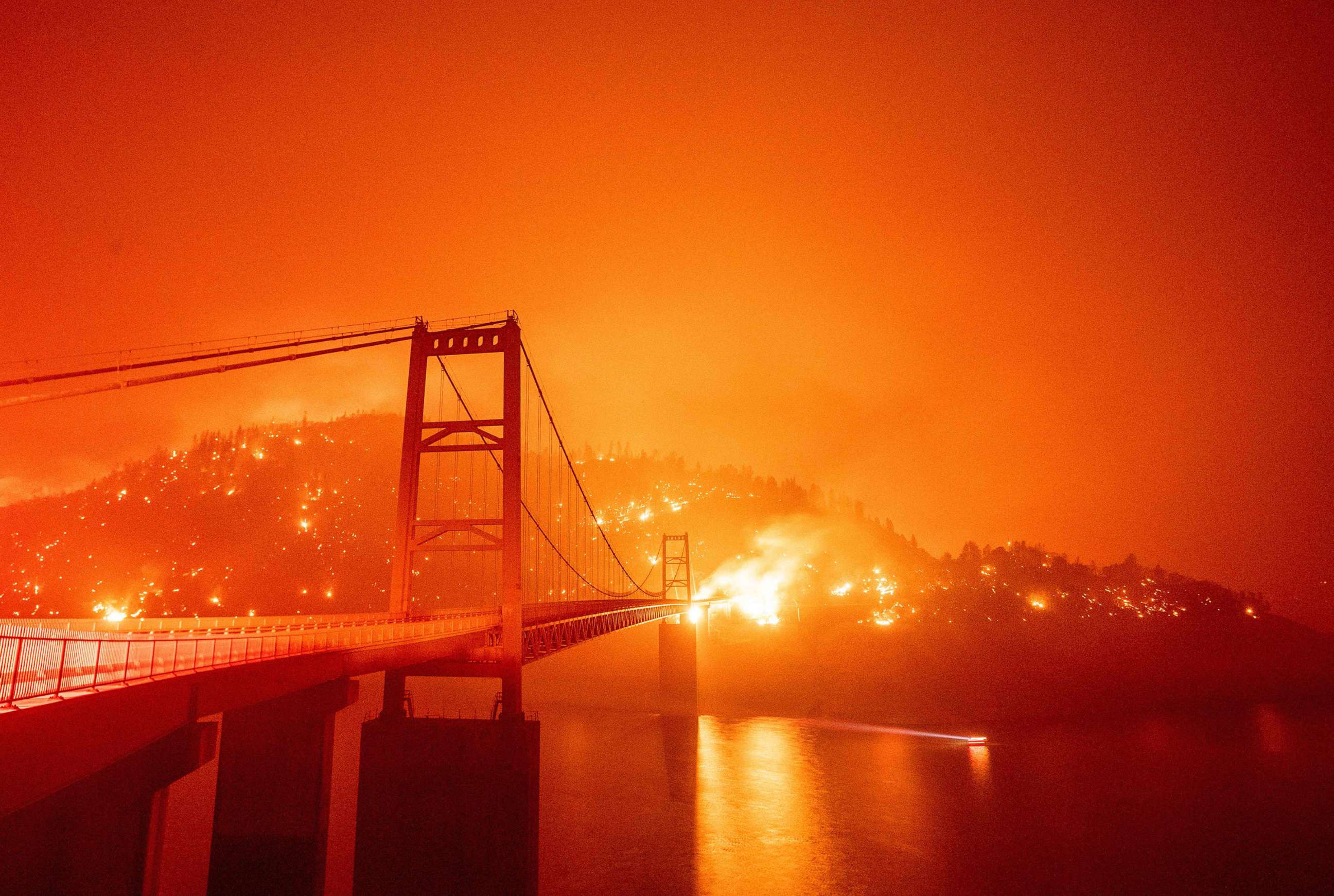 PHOTO: A boat motors by as the Bidwell Bar Bridge is surrounded by fire in Lake Oroville during the Bear fire in Oroville, Calif., on Sept. 9, 2020.