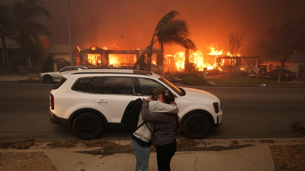 PHOTO: People embrace as they evacuate following powerful winds fueling devastating wildfires in the Los Angeles area, at the Eaton Fire in Altadena, Calif., Jan. 8, 2025.