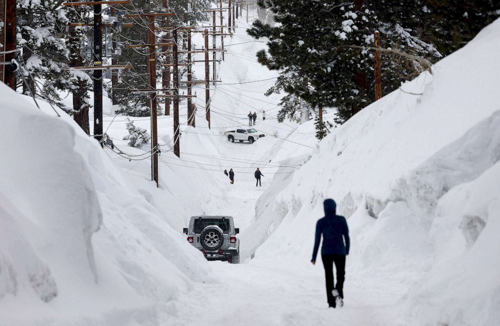 PHOTO: People make their way down a road is lined with snowbanks piled up from multiple storms, after more heavy snow fell, March 29, 2023, in Mammoth Lakes, Calif.