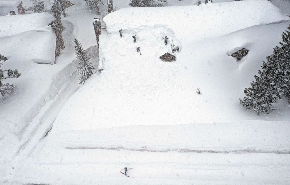 PHOTO: A skier passes by as workers remove snow from the roof of a condominium complex in the Sierra Nevada mountains after another storm system brought heavy snowfall, March 29, 2023, in Mammoth Lakes, Calif.