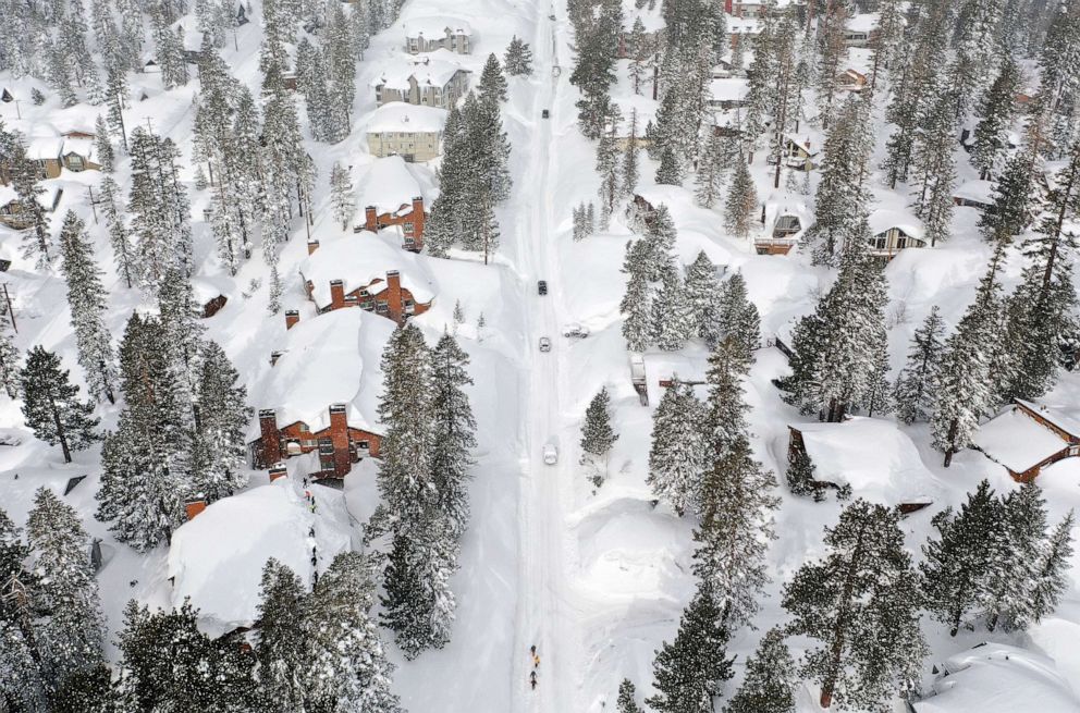 PHOTO: Snowboarders walk and cars attempt to drive in the Sierra Nevada mountains, as now reached record levels, March 29, 2023 in Mammoth Lakes, Calif.