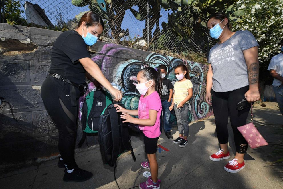 PHOTO: A volunteer hands a child a backpack filled with school supplies at a distribution to support neighborhood families, Aug. 14, 2020, in Los Angeles.
