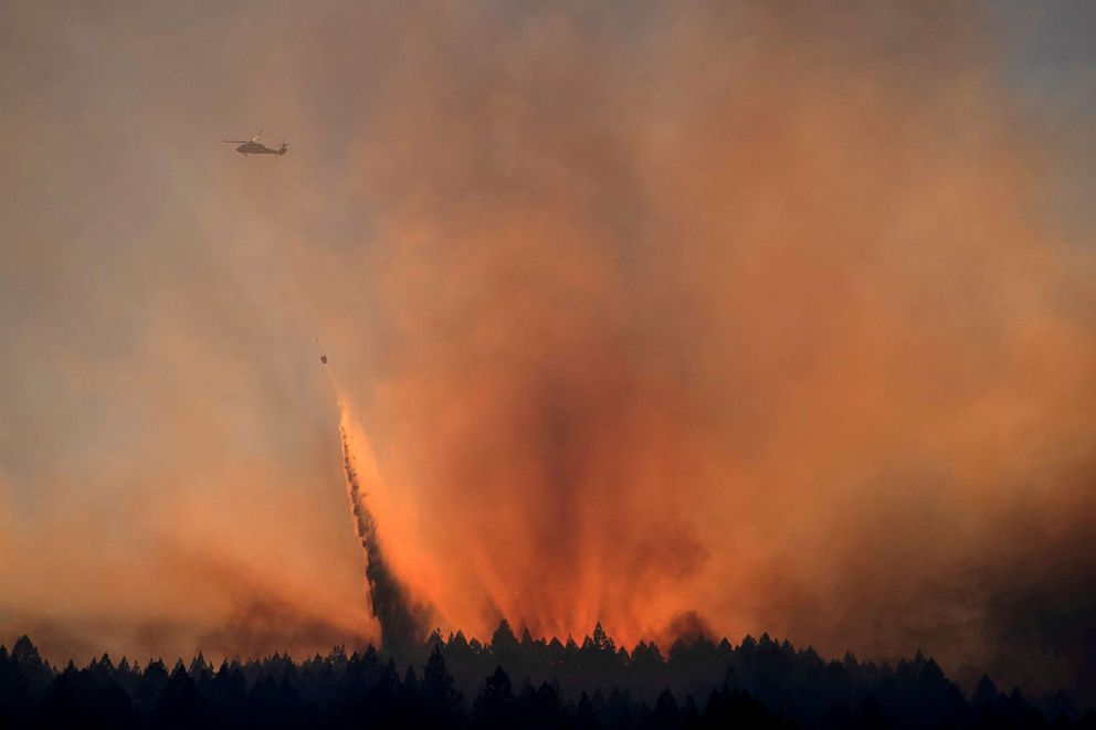 PHOTO: A helicopter is backlit by the sun setting as it drops water over the Bothe-Napa Valley State Park alight from the Glass Fire in Calistoga, Calif., Oct. 3, 2020.