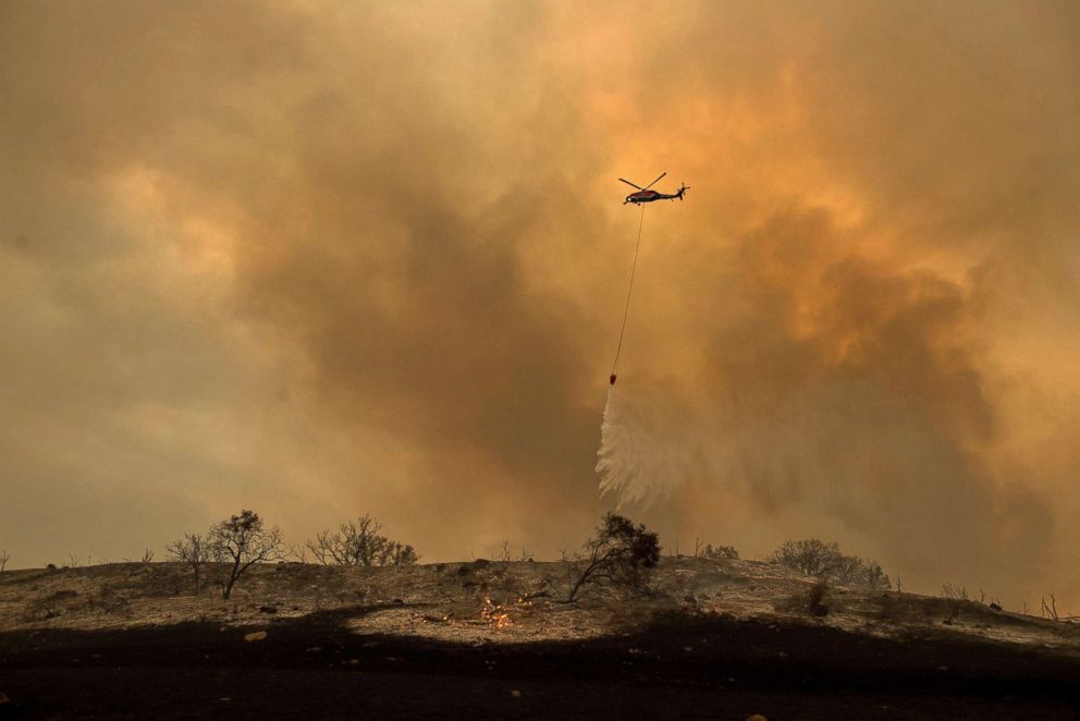 PHOTO: A helicopter drops water while trying to keep a wildfire from jumping Santa Ana Road near Ventura, Calif., Dec. 9, 2017.