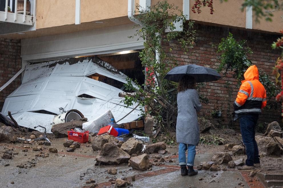 PHOTO: People stand near a garage that a landslide and flash flood smashed through in a hillside residential neighborhood, Feb. 5, 2024, in Los Angeles.