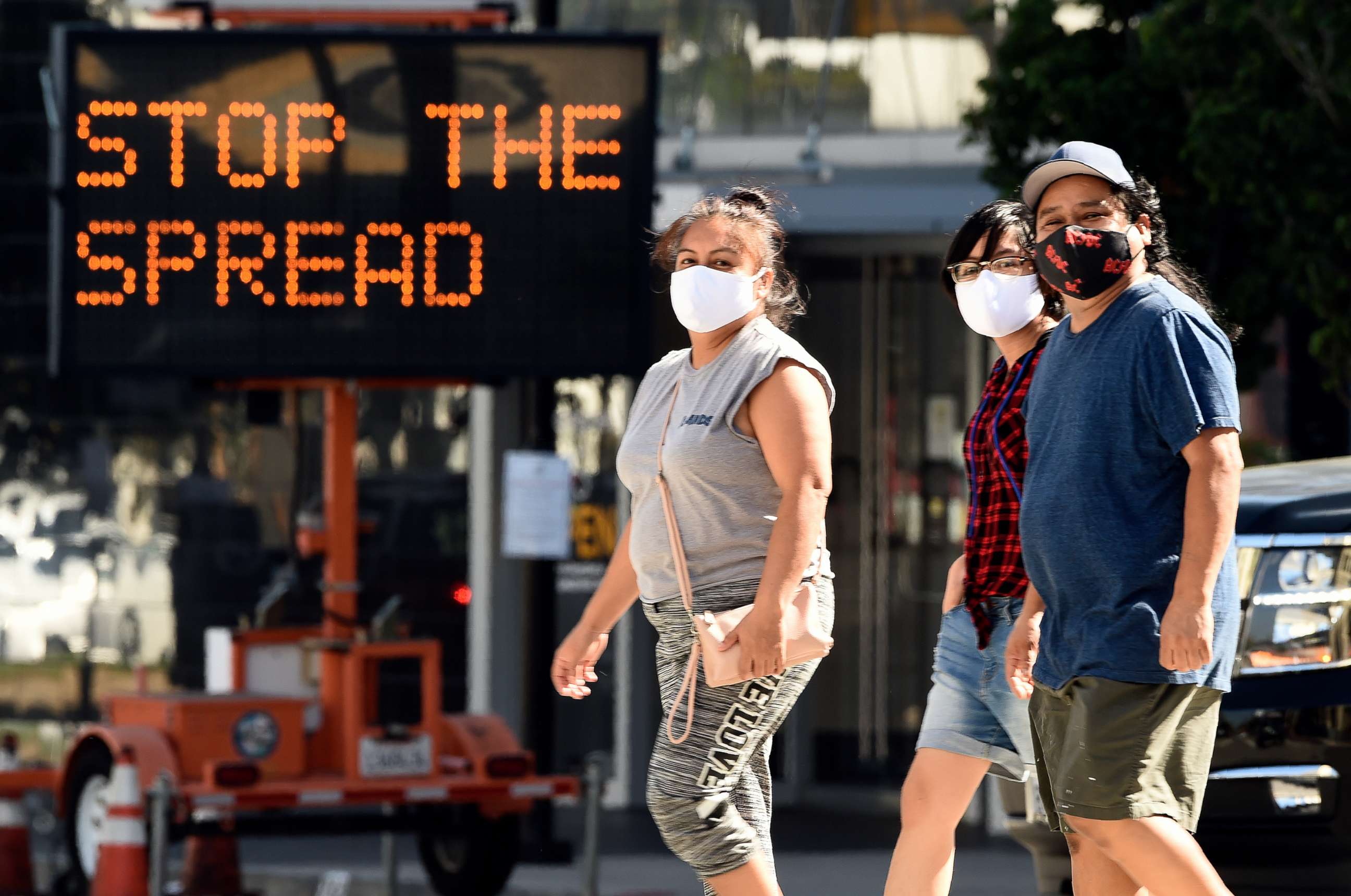 PHOTO: Pedestrians wear masks as they walk in front of a sign reminding the public to take steps to stop the spread of coronavirus, July 23, 2020, in Glendale, Calif.