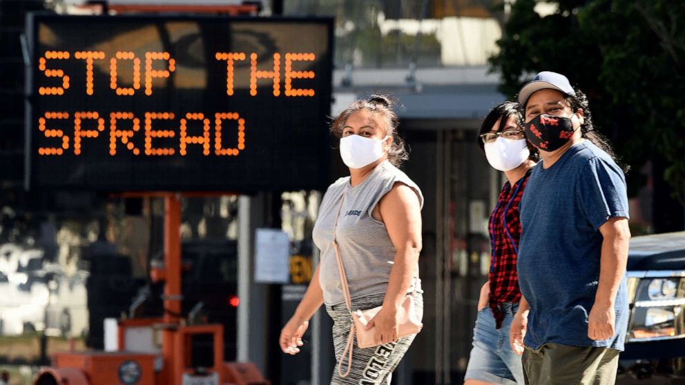 PHOTO: Pedestrians wear masks as they walk in front of a sign reminding the public to take steps to stop the spread of coronavirus, July 23, 2020, in Glendale, Calif.