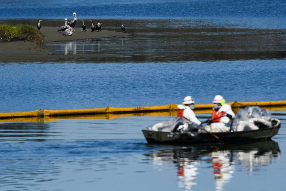 PHOTO: Environmental clean up crews wear PPE as they paddle a boat along oil containment booms to contain oil that flowed near the Talbert Marsh after an oil spill in the Pacific Ocean in Huntington Beach, Calif., Oct. 5, 2021.