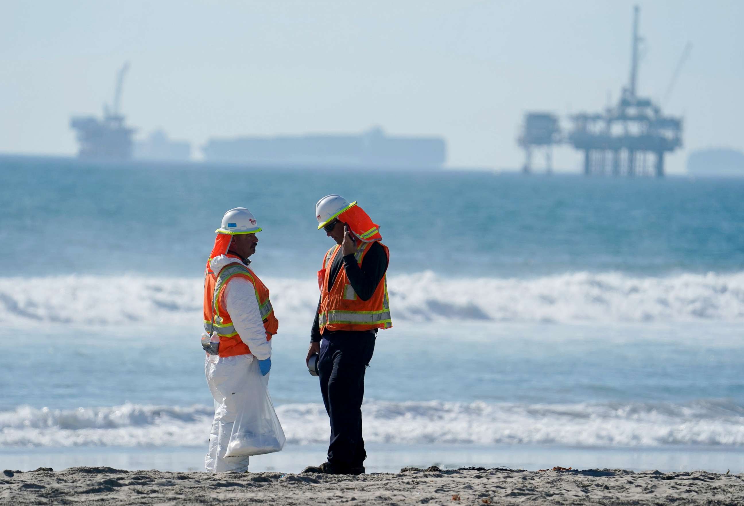 PHOTO: A cleanup crew walk along Huntington Beach looking for spots of oil north of the pier with cargo container ships in the background in Huntington Beach, Southern Calif., Oct. 6, 2021.
