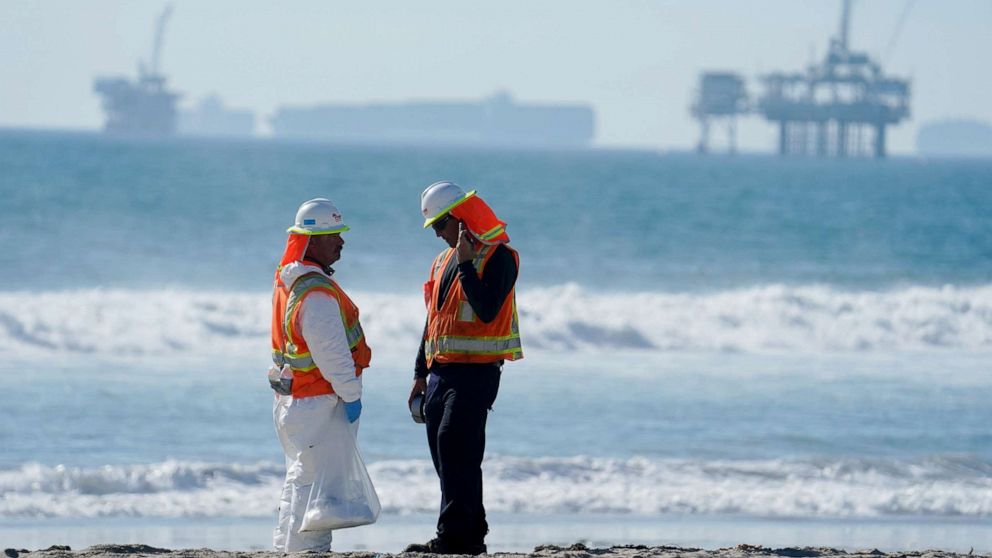 PHOTO: A cleanup crew walk along Huntington Beach looking for spots of oil north of the pier with cargo container ships in the background in Huntington Beach, Southern Calif., Oct. 6, 2021.