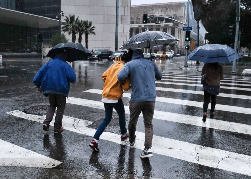 PHOTO: Pedestrians huddle under umbrellas while trying to make their way across a street in the rain in Los Angeles, March 21, 2018. 