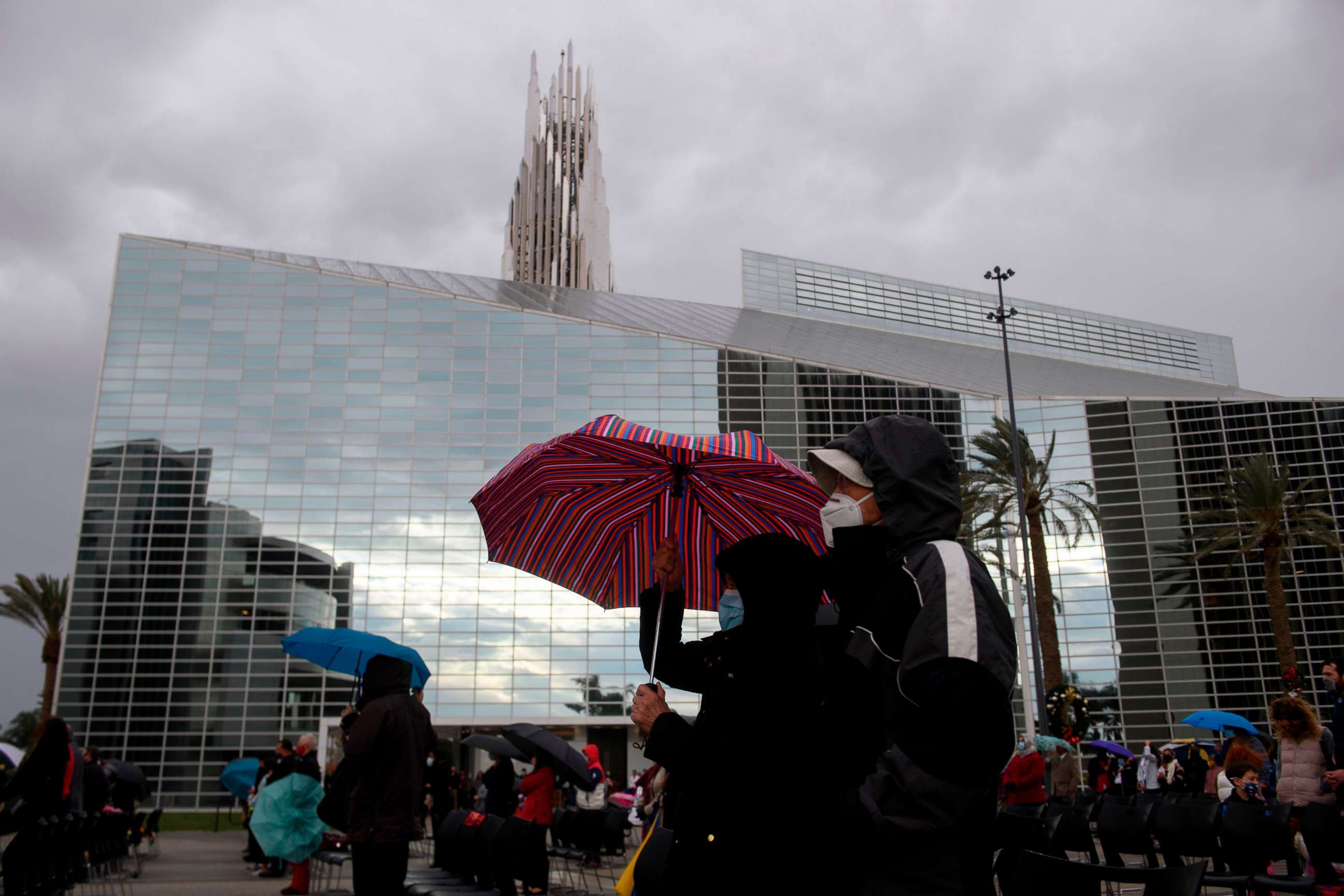 PHOTO: People wear masks and carry umbrellas in the rain, while social distancing due to COVID-19, during a Christmas Eve Roman Catholic Mass at Christ Cathedral on Dec. 24, 2020 in Garden Grove, Calif.