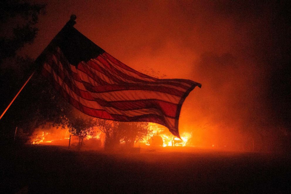 PHOTO: An American flag blows in the wind in front of a burning home in Vacaville, Calif., during the LNU Lightning Complex fire, Aug. 19, 2020.