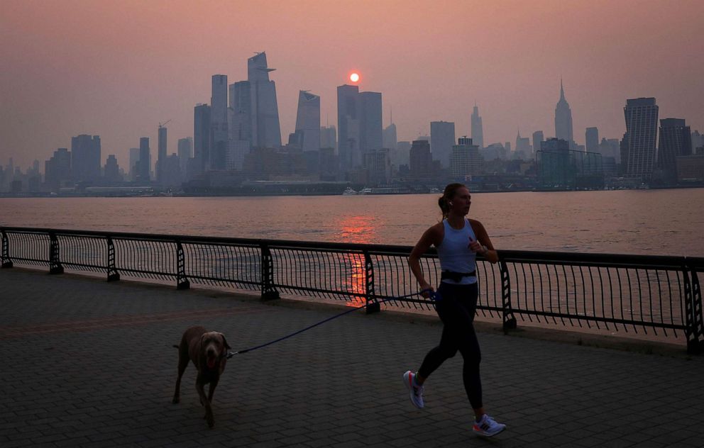 PHOTO: A woman jogs with a dog along the Hudson River shortly after sunrise, as haze and smoke caused by wildfires in Canada hang over the Manhattan skyline, in New York City, June 7, 2023.