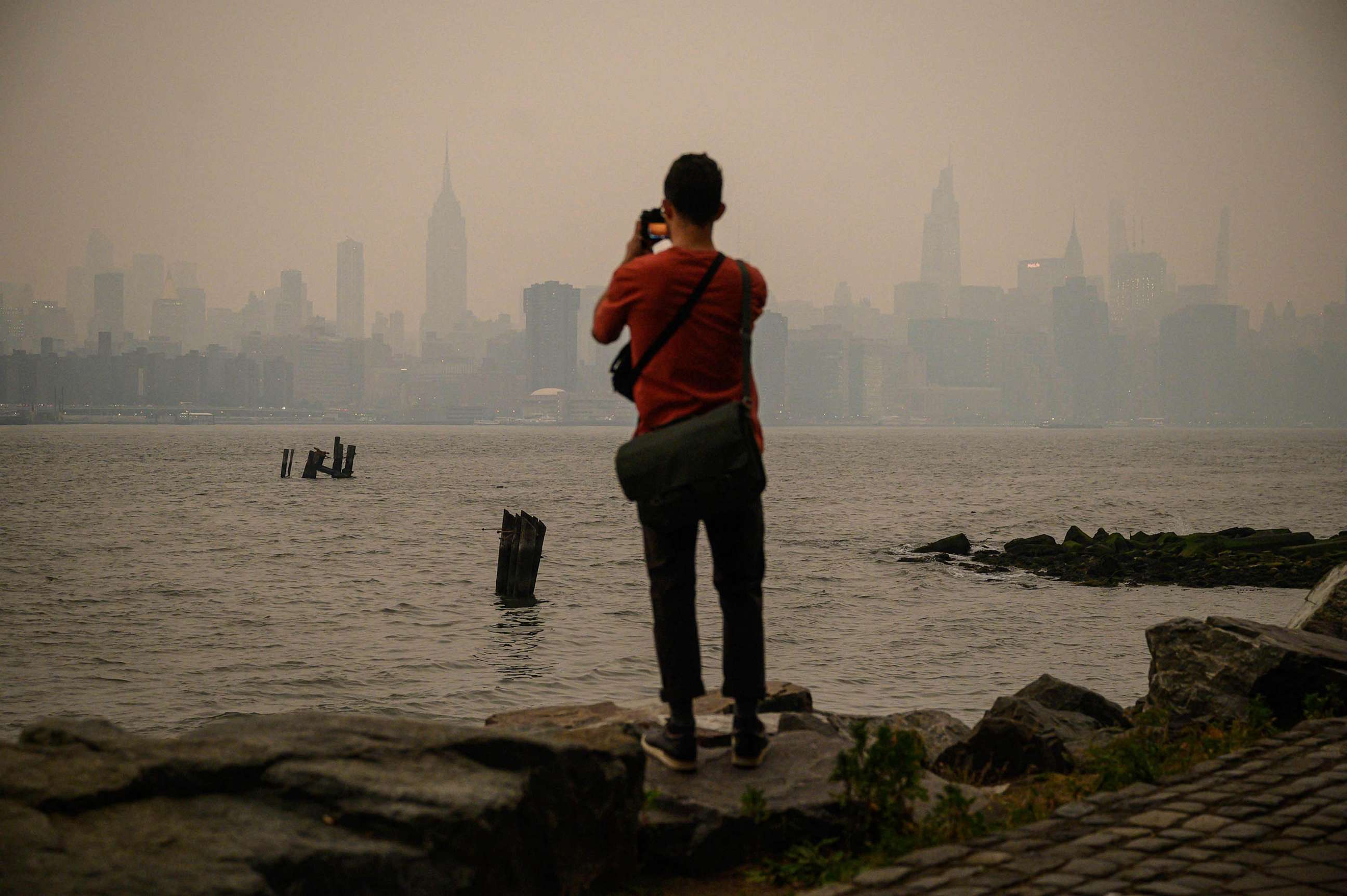 PHOTO: A man stands before the New York city skyline and east river shrouded in smoke, in Brooklyn, June 6, 2023.