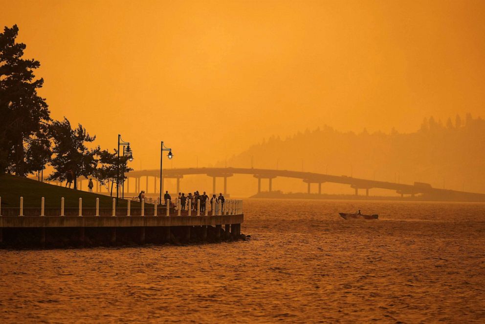 PHOTO: A person travels in a boat past people walking on the boardwalk as smoke from the McDougall Creek wildfire blankets the area on Okanagan Lake in Kelowna, British Columbia, Aug. 18, 2023.