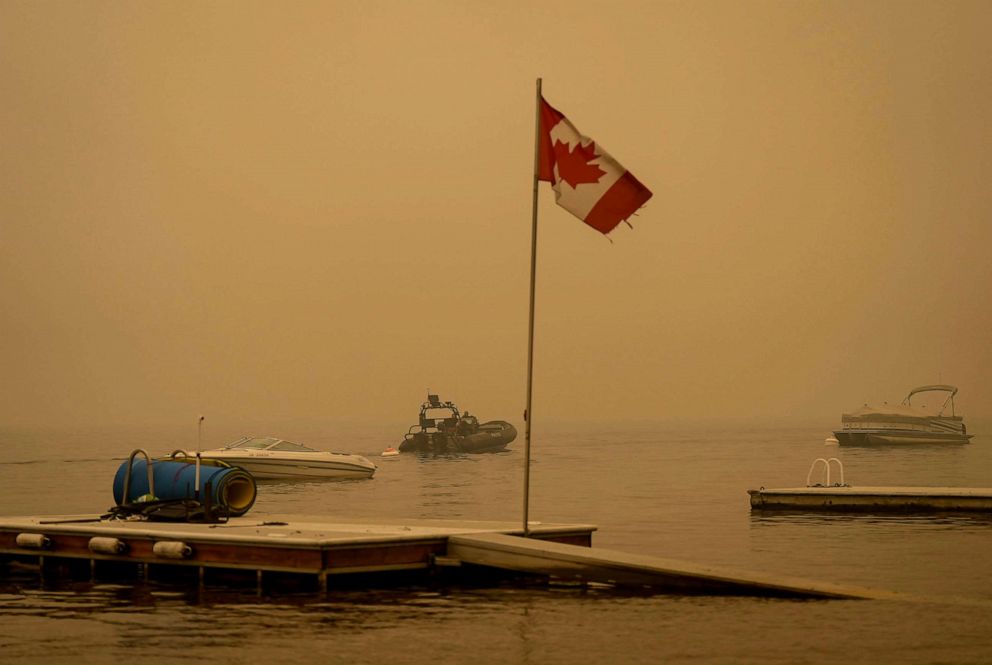 PHOTO: Thick smoke from the Lower East Adams Lake wildfire fills the air around a Canadian flag fluttering in the wind as Royal Canadian Mounted Police officers on a boat patrol Shuswap Lake, in Scotch Creek, British Columbia, Aug. 20, 2023.