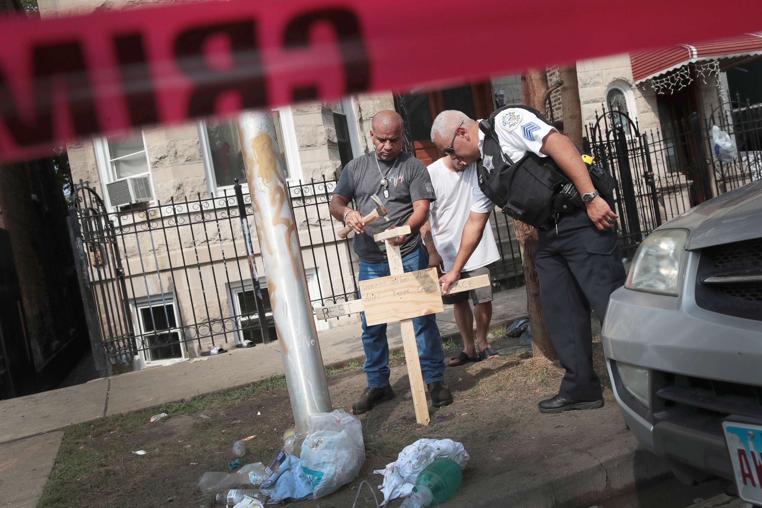 PHOTO: A police officer helps as Omar Acevedo pounds a cross bearing the names of victims into the dirt outside a home where eight people perished, including six children, Aug. 26, 2018, in Chicago.