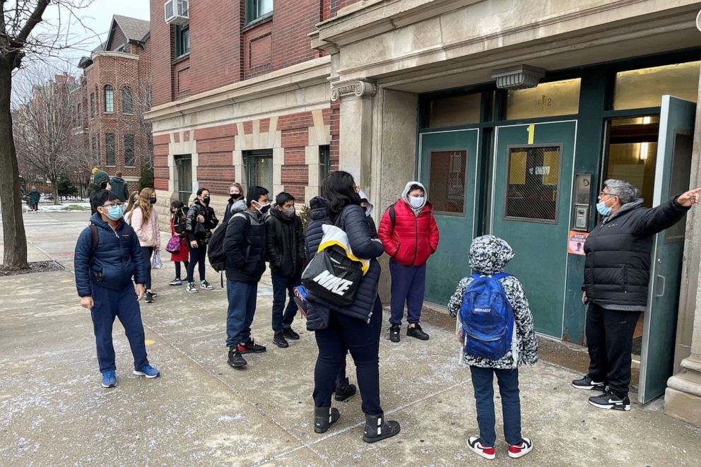 PHOTO: Students wearing face masks line up outside the entrance of Prescott Elementary School while directed by school staff in Chicago, Jan. 12, 2022.