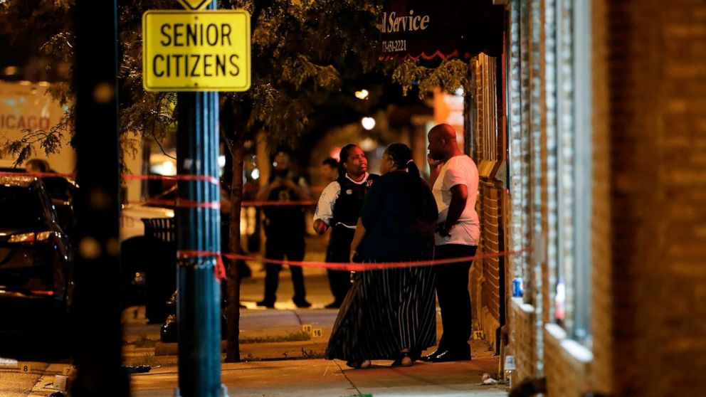 PHOTO: A Chicago police officer talks with people in front of Rhodes Funeral Services as evidence markers are seen on the ground at the scene of a shooting in Chicago, July 21, 2020.
