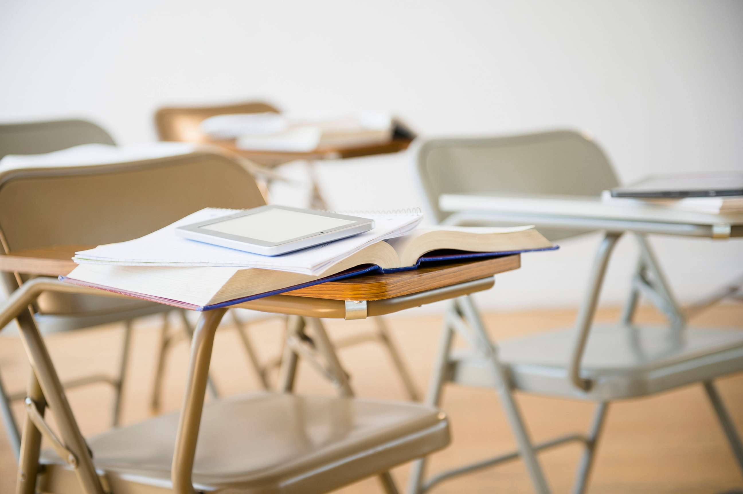 PHOTO: Digital tablet and book on desk in classroom. empty desks