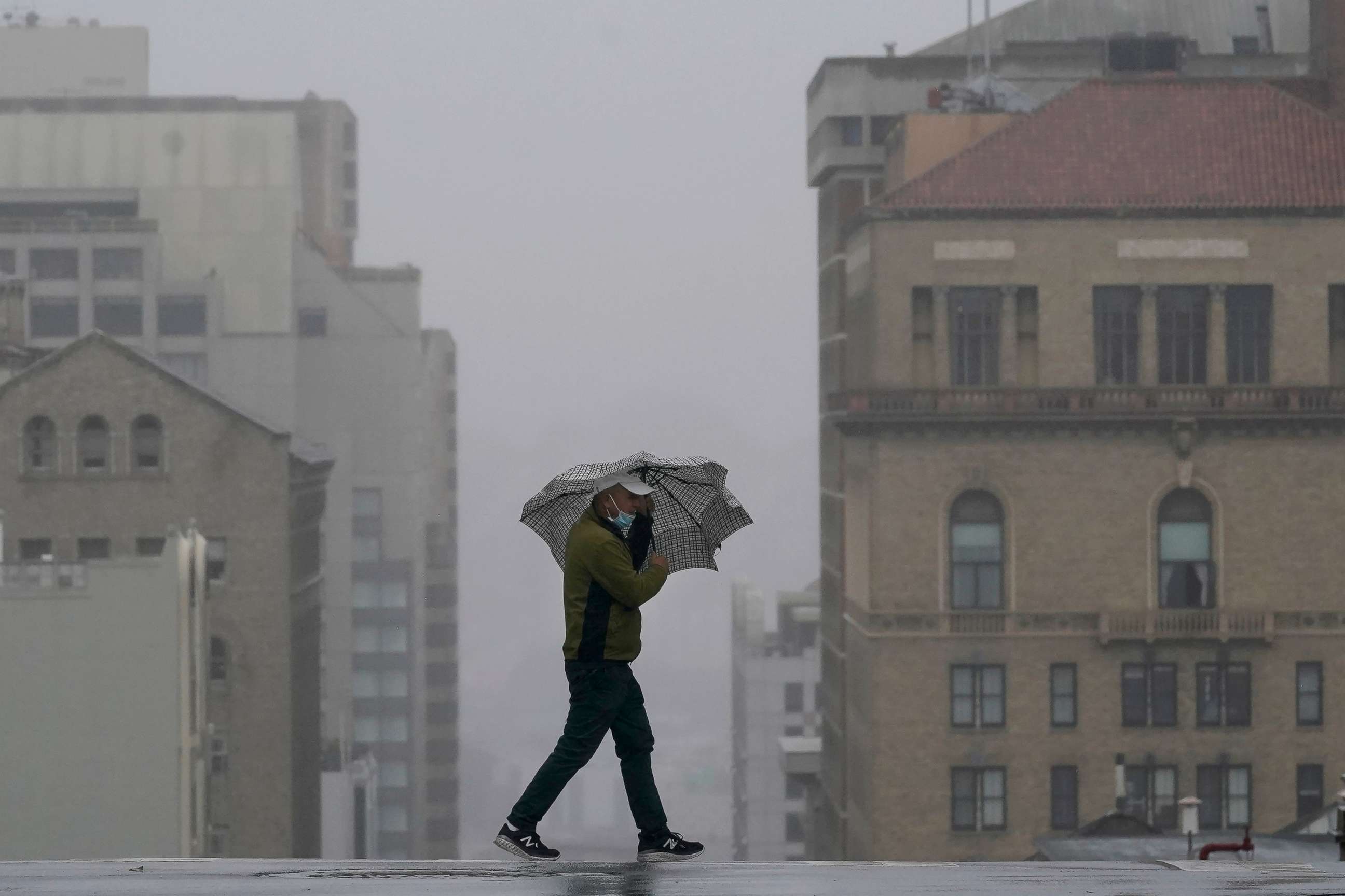 PHOTO: A man walks with an umbrella while crossing a street in San Francisco, Tuesday, Nov. 17, 2020. A new weather system carrying rain and snow headed into Northern California on Tuesday. 