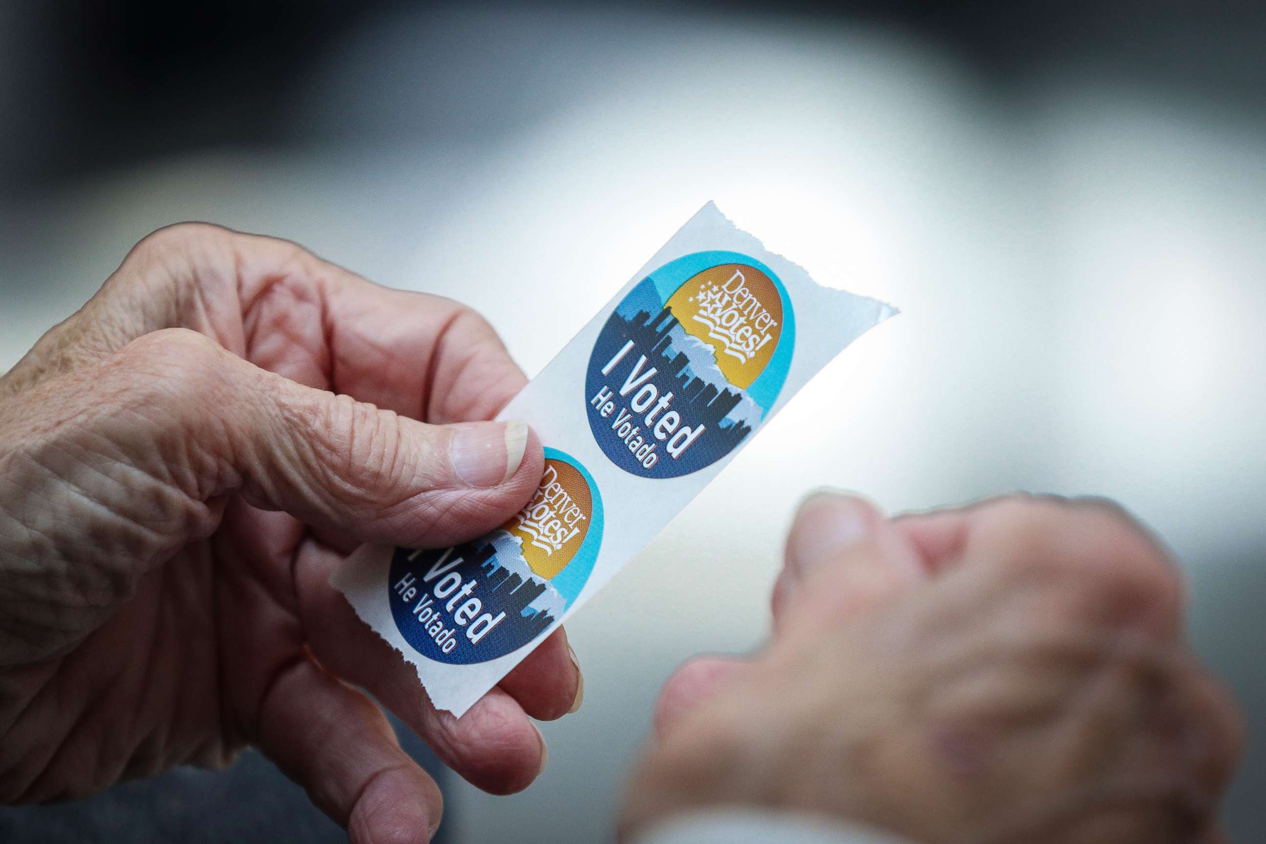 PHOTO: An election judge tears off a couple of "I Voted" stickers to hand to a voter as people cast their ballots in the State Primaries on June 28, 2022 at the Wellington E. Webb Municipal Office Building in Denver.