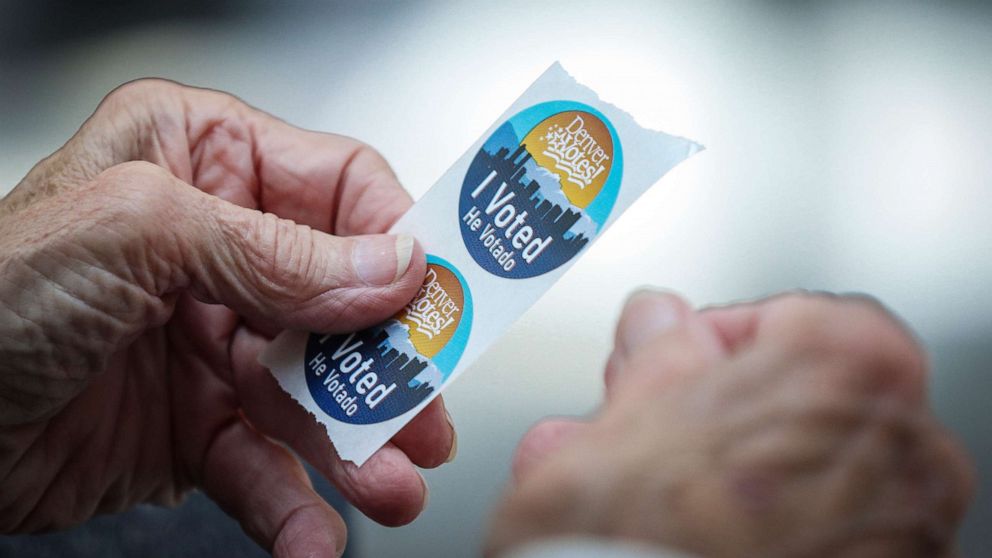 PHOTO: An election judge tears off a couple of "I Voted" stickers to hand to a voter as people cast their ballots in the State Primaries on June 28, 2022 at the Wellington E. Webb Municipal Office Building in Denver.