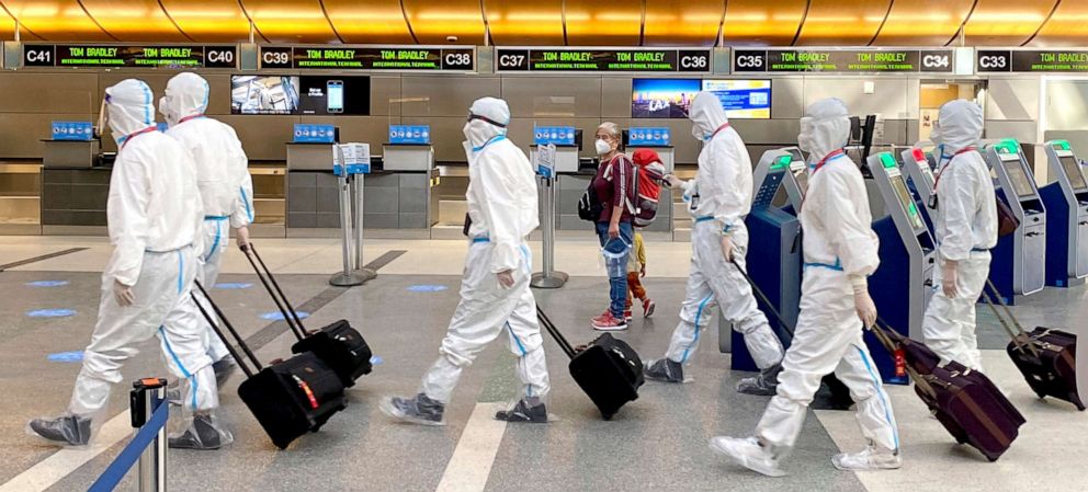 PHOTO: A woman, accompanied by a child, looks over as an airline crew wearing full personal protective equipment against COVID-19 walks through the international terminal at Los Angeles International Airport in Los Angeles on  Nov. 17, 2020.