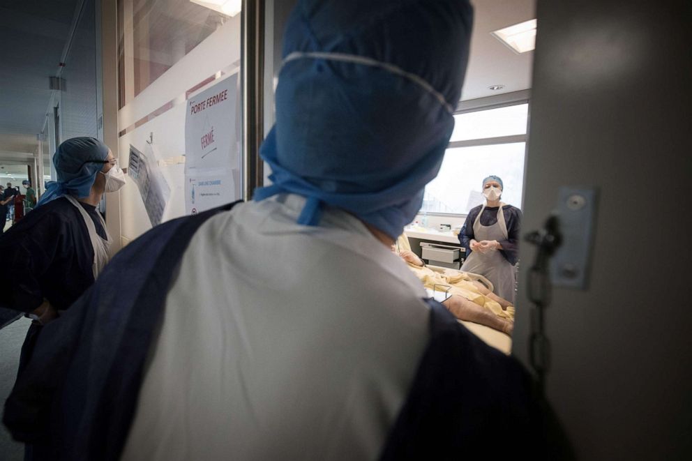 PHOTO: Medical workers look inside a room as another tends to a patient infected with COVID-19 stand up at the intensive care unit of a public hospital in Paris on April 27, 2020.