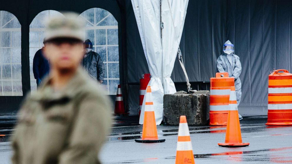 PHOTO: Medical professionals in protective suits wait to take information from people at a new drive-through COVID-19 mobile testing center in New Rochelle, N.Y., March 13, 2020.