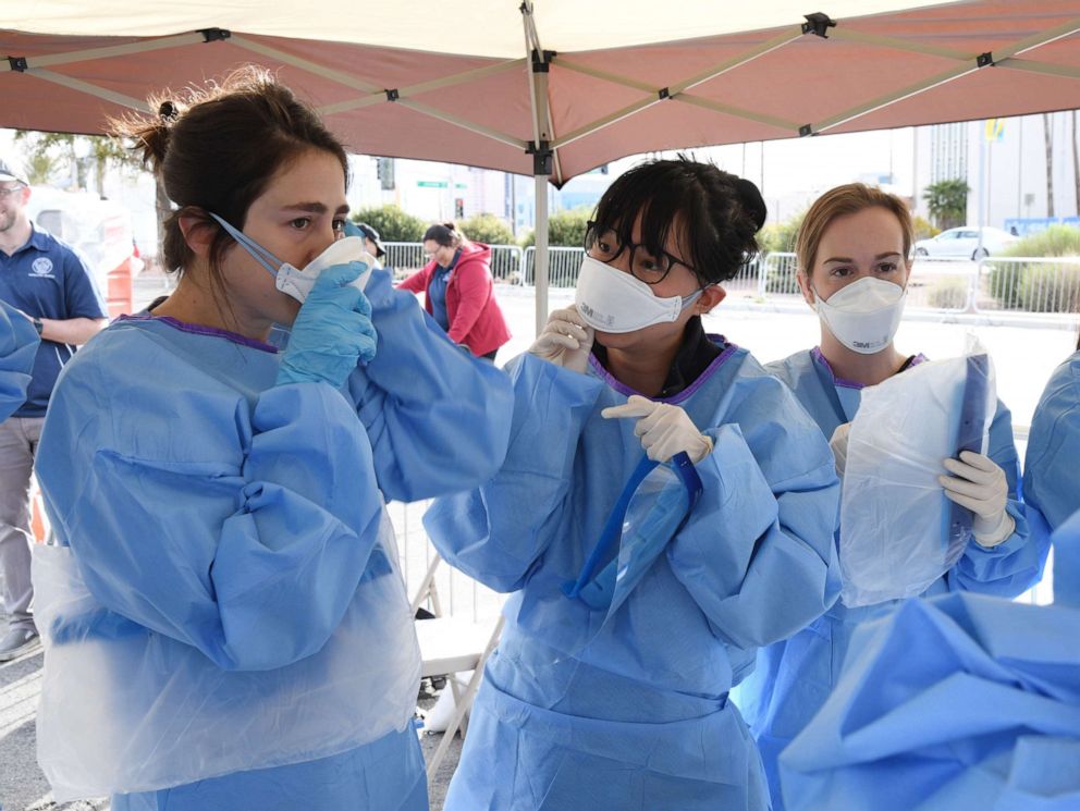 PHOTO: (L-R) Touro University Nevada medical students Allison Moran, Claire Chen and Miranda Stiewig put on personal protective equipment as they get ready to conduct medical screenings at a temporary homeless shelter at Cashman Center on March 28, 2020.