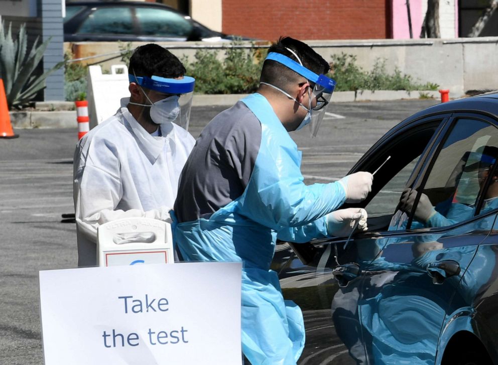 PHOTO: Workers wearing personal protective equipment gather the tests administered as Mend Urgent Care hosts a drive-thru testing for COVID-19 at the Westfield Fashion Square in the Sherman Oaks neighborhood of Los Angeles, California, on April 14, 2020.