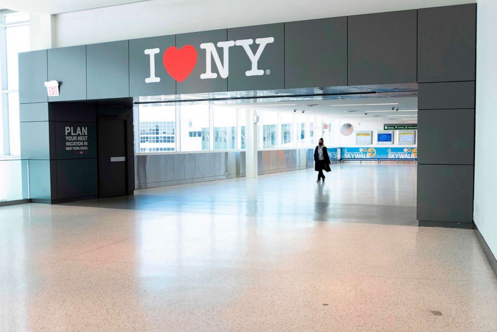 PHOTO: A woman wearing a mask walks past a sing reading "I heart NY" at  Terminal 5 of  John F. Kennedy Airport (JFK) amid the novel coronavirus pandemic on May 13, 2020 in Queens, N.Y.