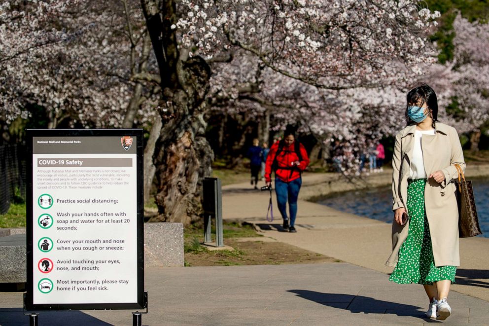 PHOTO: A woman wearing a mask stops to read coronavirus safety tips along an almost empty Tidal Basin lined with cherry blossoms that are about to peak, March 18, 2020, in Washington, D.C.