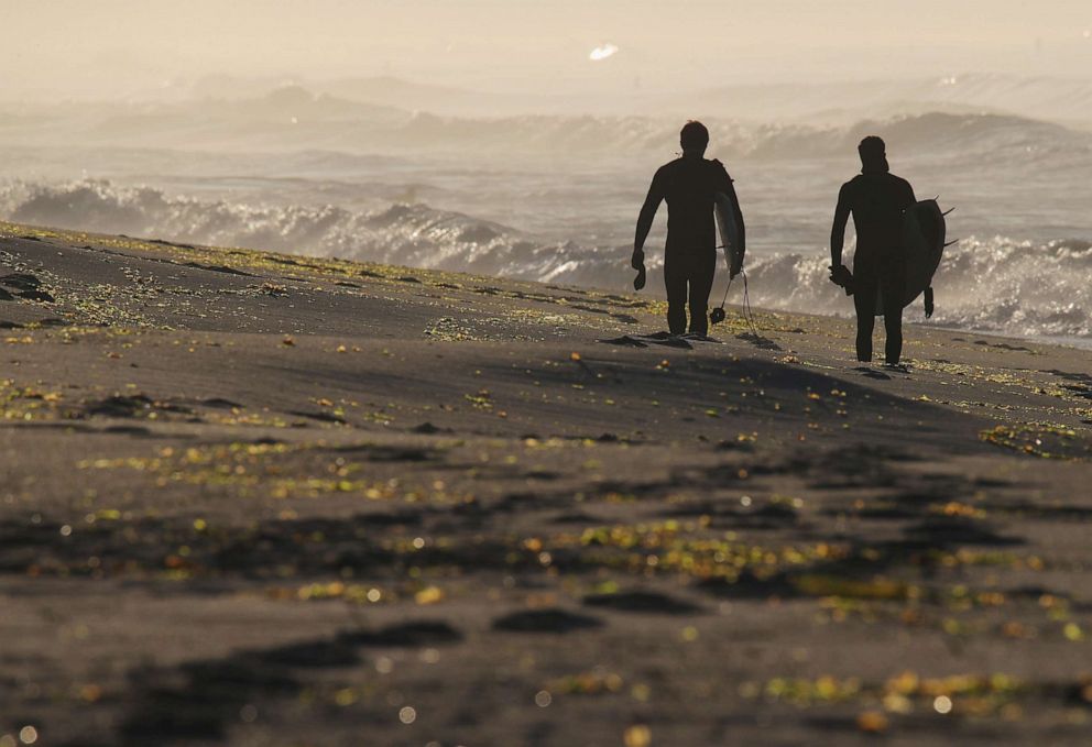 PHOTO: Surfers head to the beach in the early morning hours on April 25, 2020 in Long Beach, N.Y.
