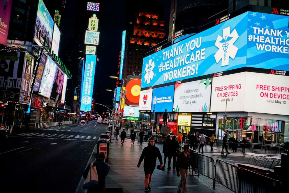 PHOTO: People walk round Times Square as some screens are illuminated in blue as part of the "Light It Blue" initiative to honor healthcare workers, during the outbreak of the coronavirus disease (COVID-19), in New York City, April 23, 2020.