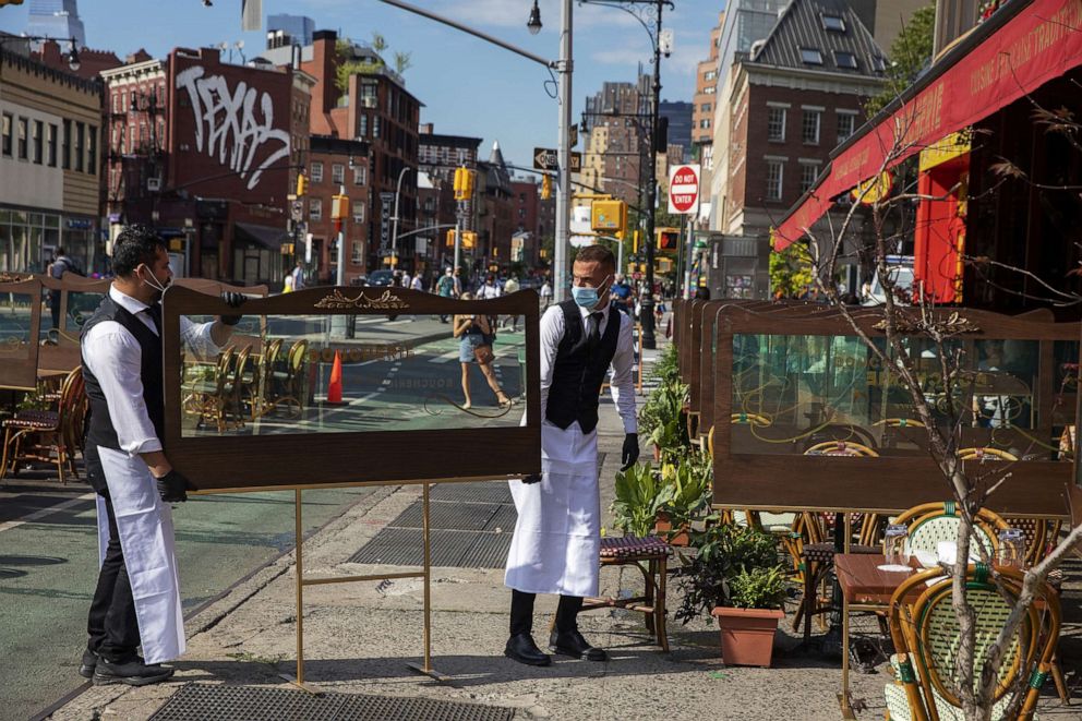 PHOTO: Waiters at a restaurant adjust social distancing screens outside for outdoor seating seating that follows current health guidelines to slow the spread of Coronavirus (COVID-19) at a restaurant in New York City, June 25, 2020.