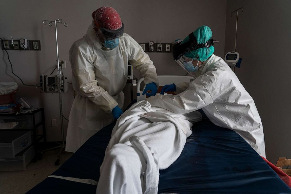 PHOTO: Medical staff wears full PPE as they wrap a deceased patient with bed sheets and a body bag in the Covid-19 intensive care unit at the United Memorial Medical Center on June 30, 2020 in Houston.