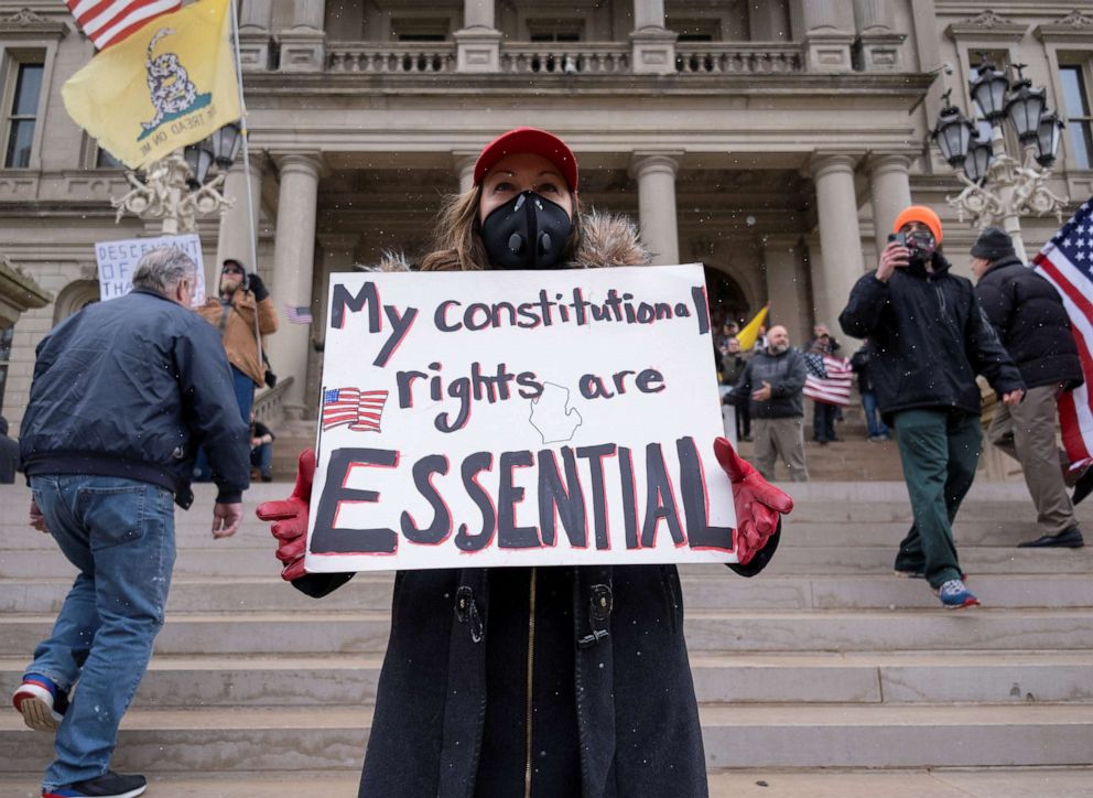 PHOTO: A woman wearing a face mask holds a placard as hundreds of supporters of the Michigan Conservative Coalition protest against the state's extended stay-at-home order in Lansing, Mich., April 15, 2020.