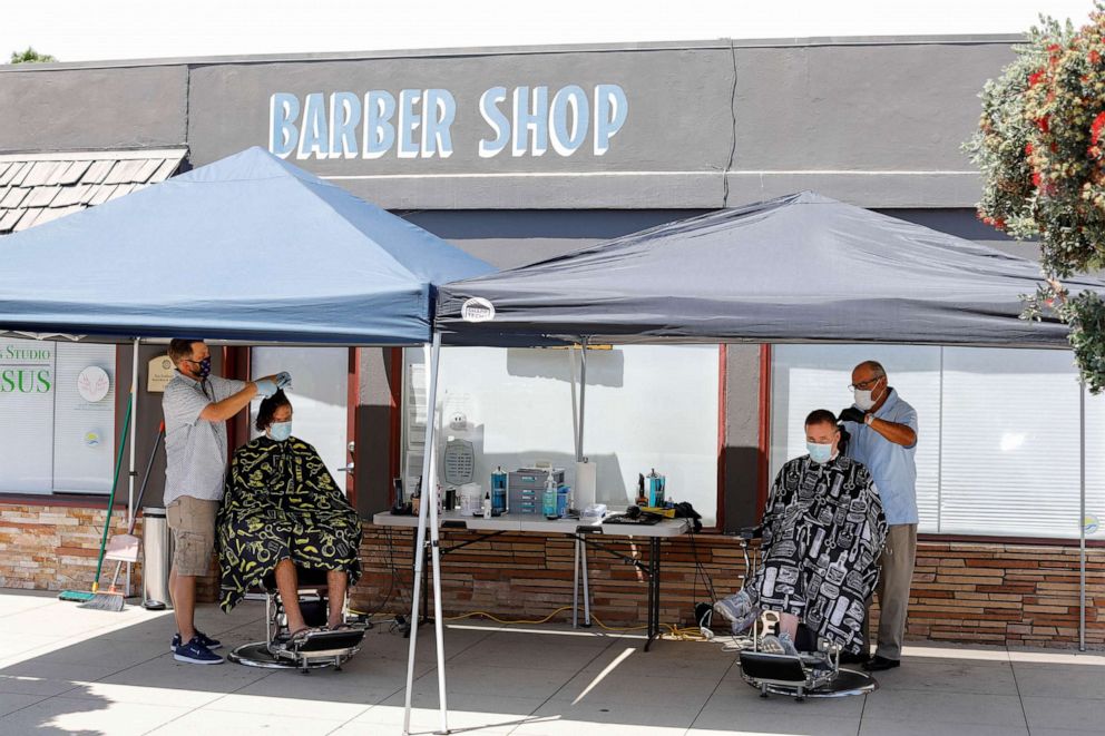 PHOTO: Barbers Nicolas Downs and Bob Castro cut customers hair from the sidewalk in front of Downs' barber shop during the outbreak of the coronavirus disease (COVID-19) in Solana Beach, Calif., July 21, 2020.