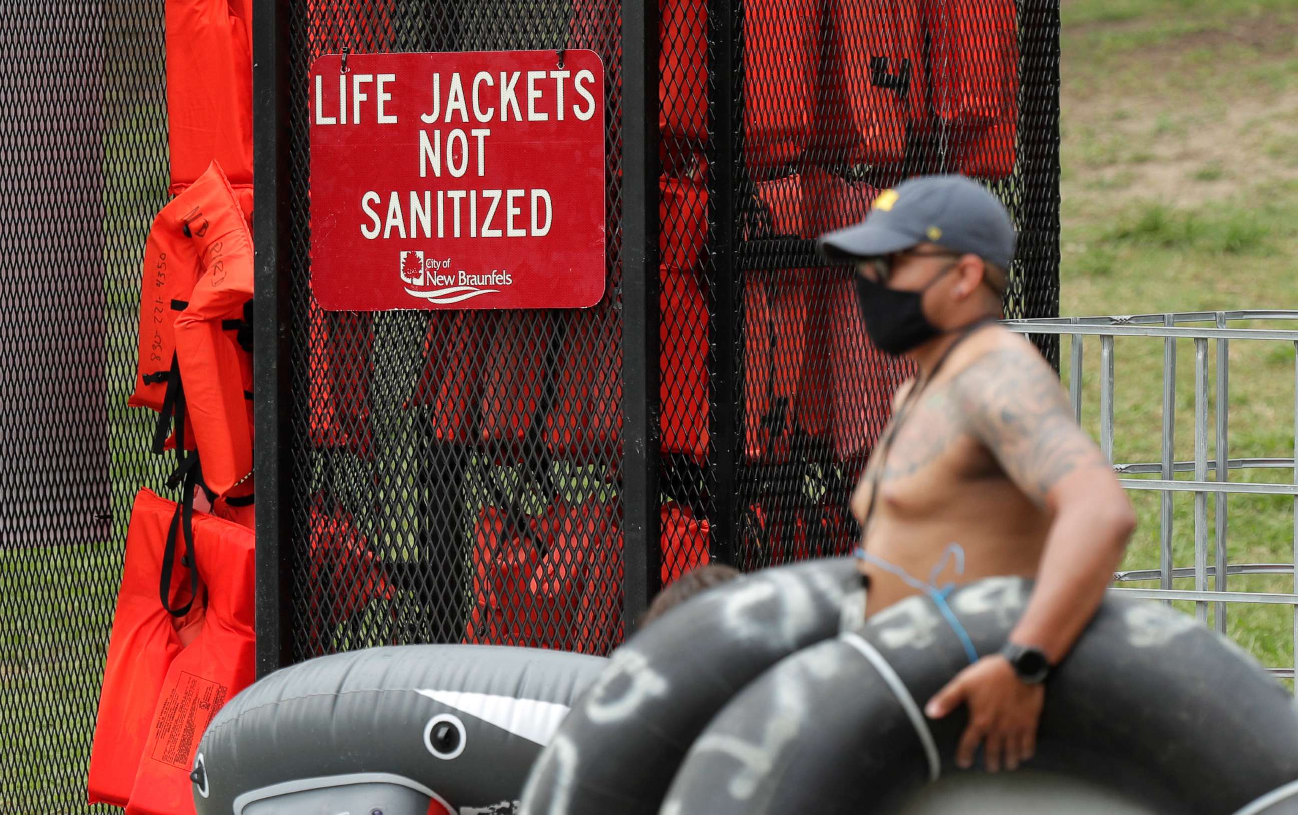 PHOTO: A tuber, wearing a mask to protect against the spread of COVID-19, passes a rack of life jackets as he prepares to float the Comal River, June 25, 2020, in New Braunfels, Texas.